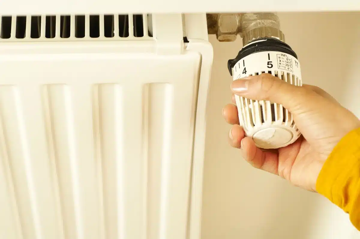 Main réglant un thermostat de chauffage pour réduire la consommation énergétique
