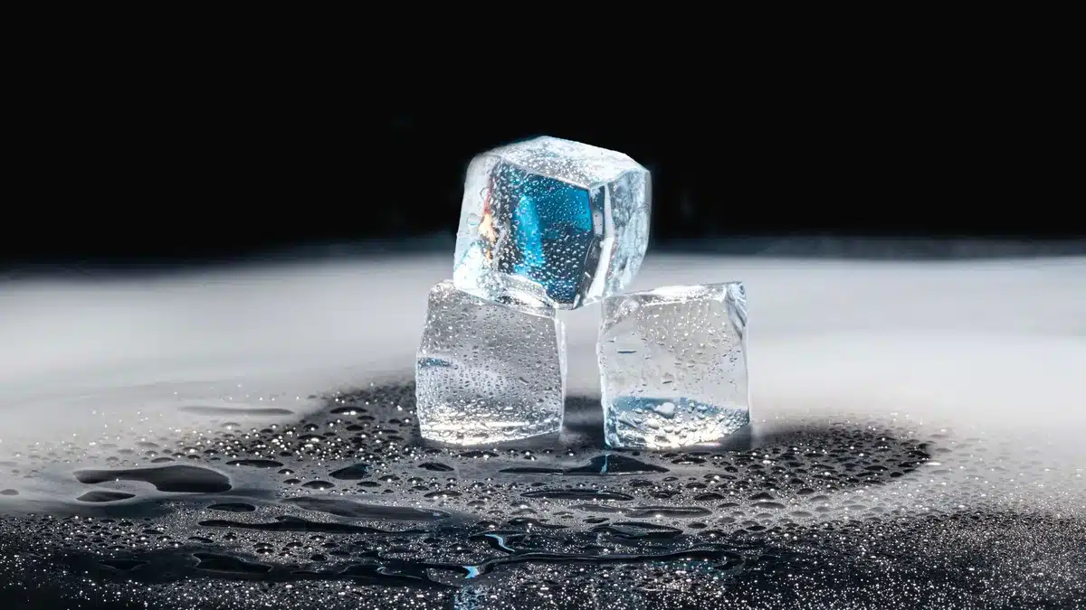 Mains versant de l'eau chaude dans un récipient à l'intérieur d'un réfrigérateur en cours de dégivrage
