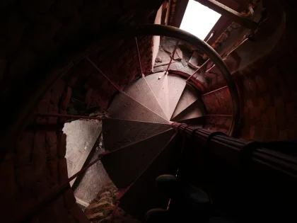 Mains tenant la rampe d'un escalier étroit en bois dans une vieille maison