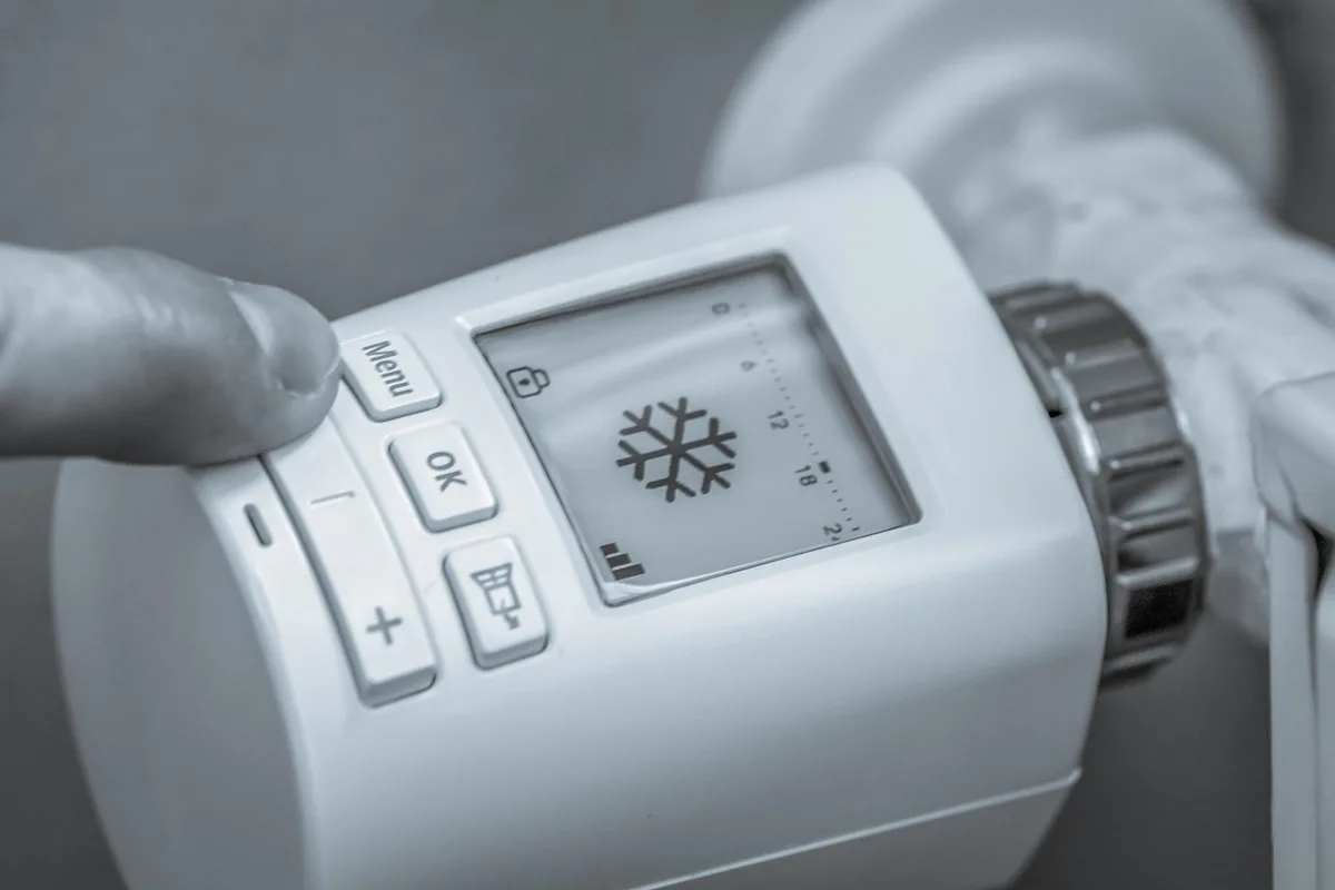 Main ajustant un thermostat près d'une unité de chauffage
